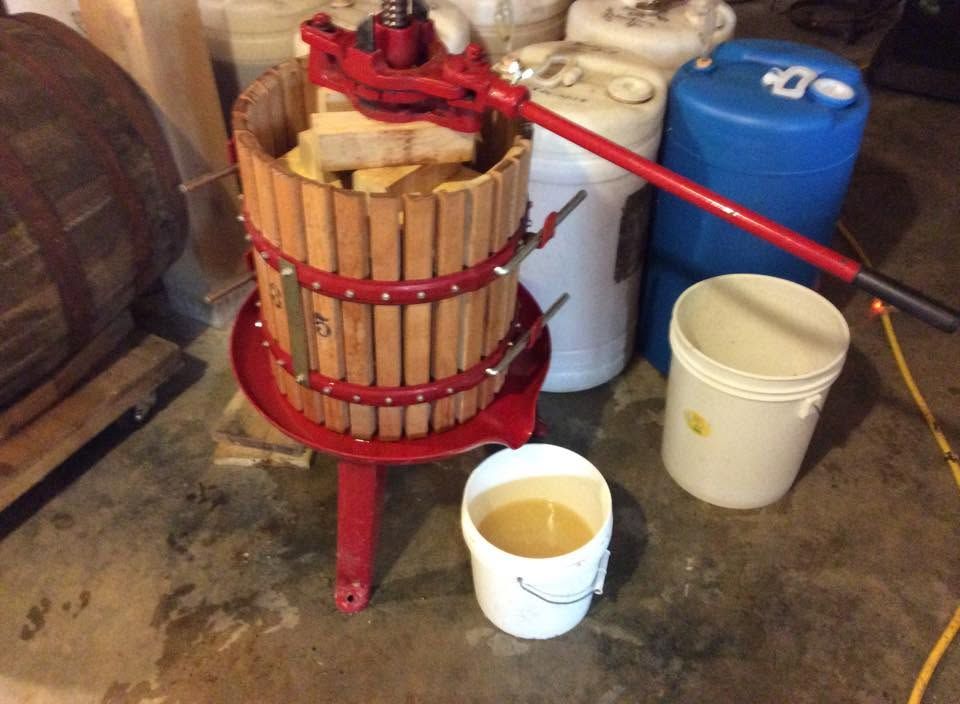 Red fruit press over bucket in a workshop, with a white pail and blue container nearby.