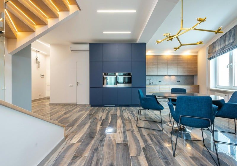 Cuisine et salle à manger modernes à aire ouverte avec chaises bleues, parquet et éclairage d'escalier
