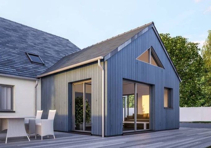 Extérieur d'une maison moderne bleu-gris avec de grandes fenêtres et une terrasse en bois à la lumière du jour