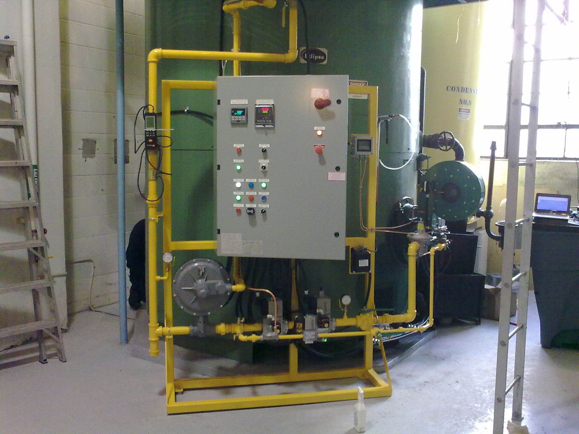 A control panel is surrounded by yellow pipes in a room