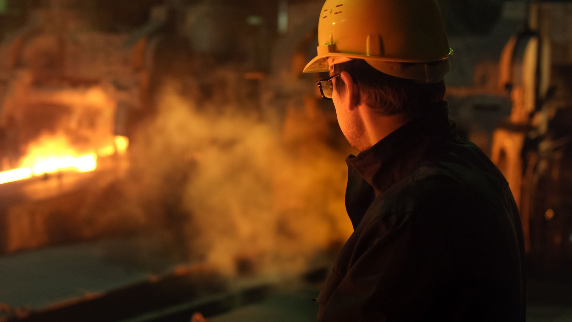 Un homme portant un casque et des lunettes se tient devant un incendie dans une usine.