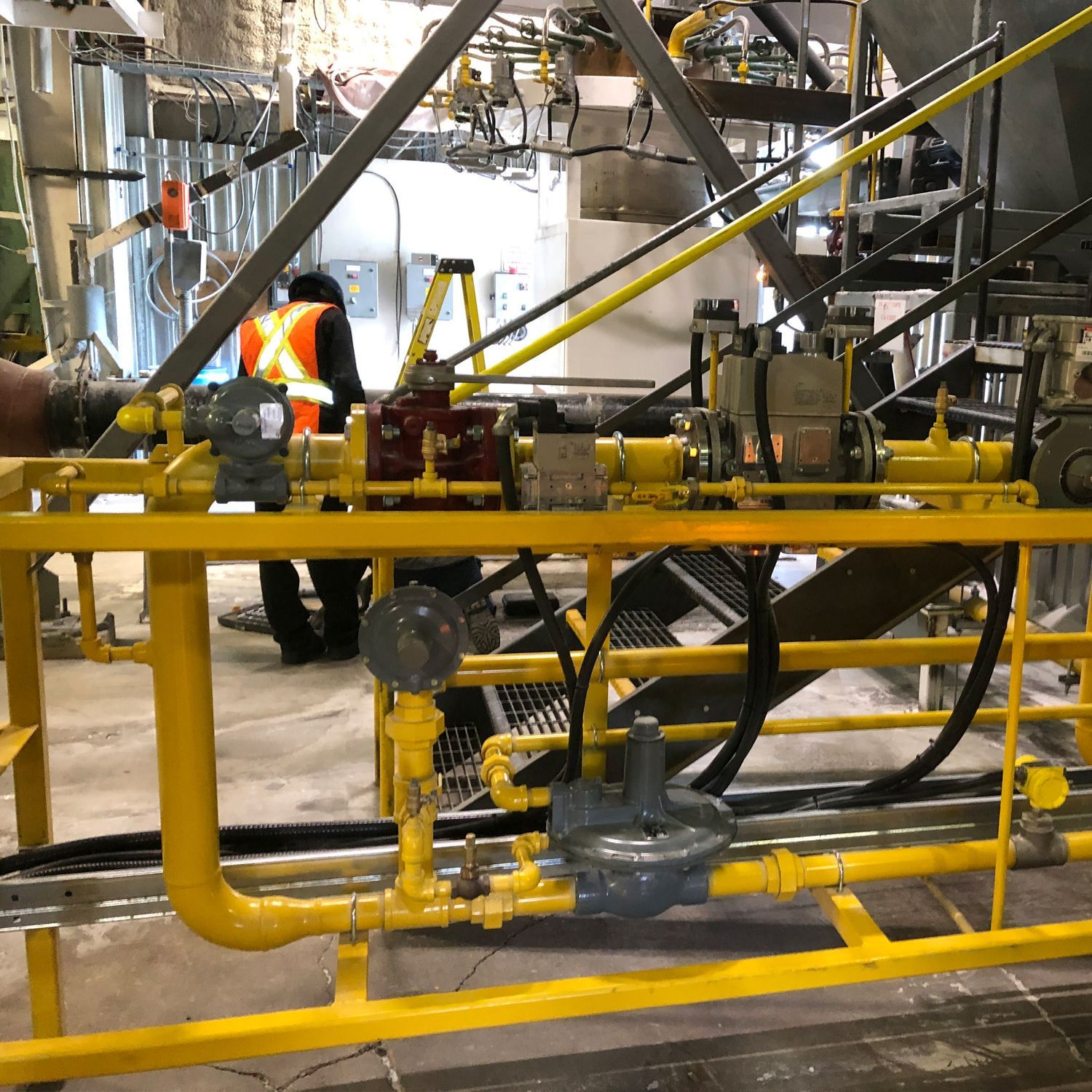 A man in a safety vest is working on a yellow pipe system