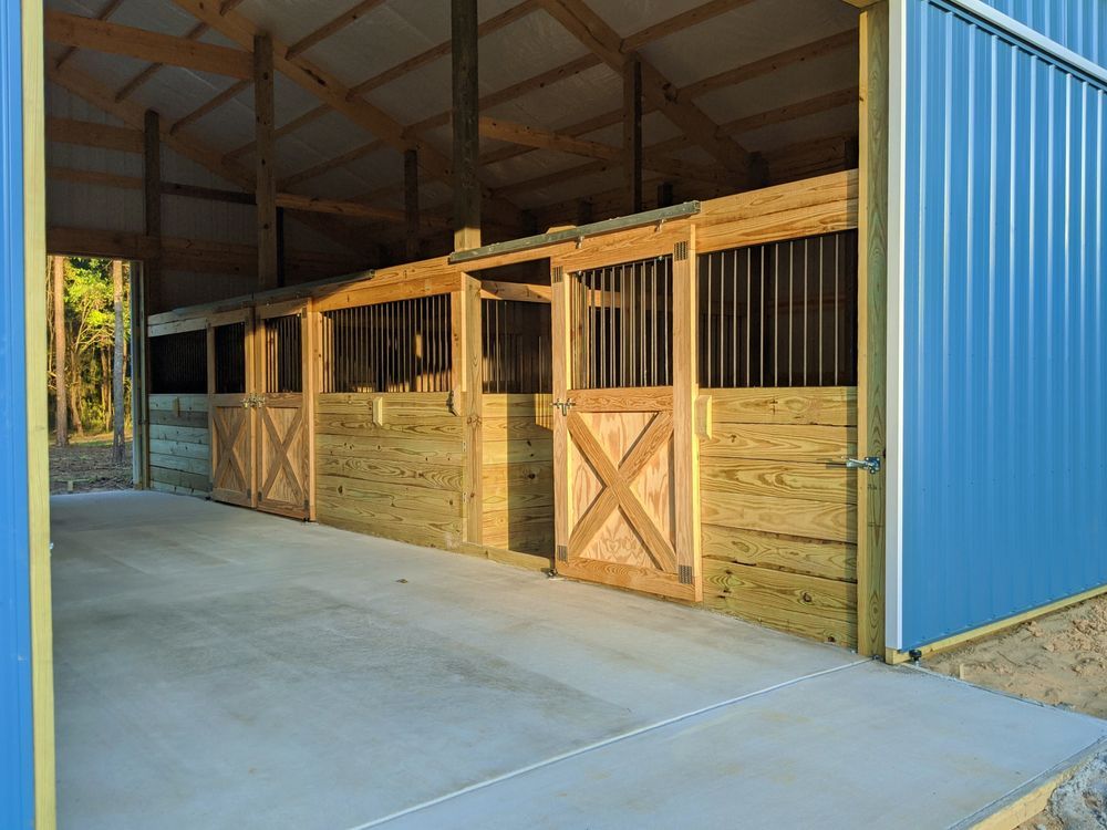 Horse stables with wooden stalls under a blue metal roof in an open-sided barn.