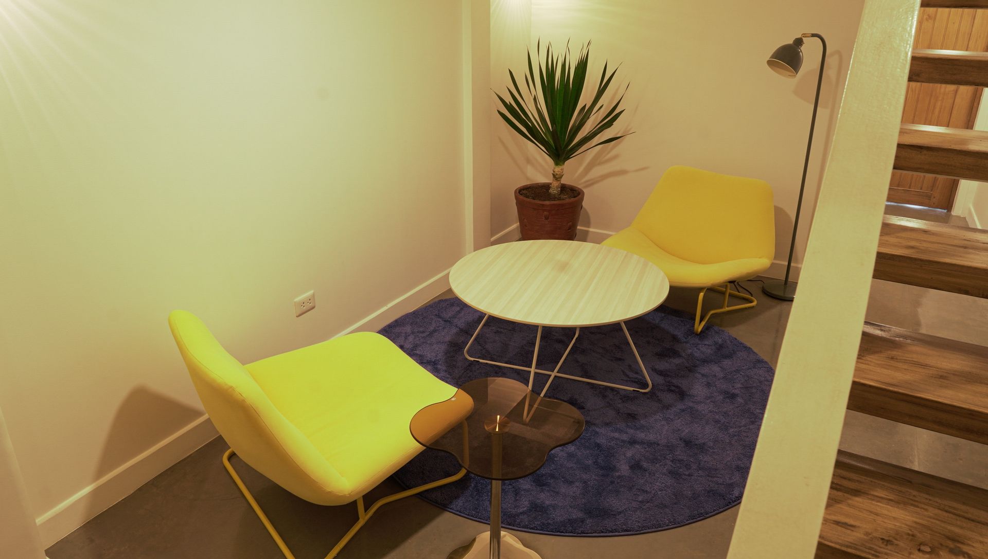 Cozy sitting area with two yellow chairs, round white table, blue rug, and potted plant.