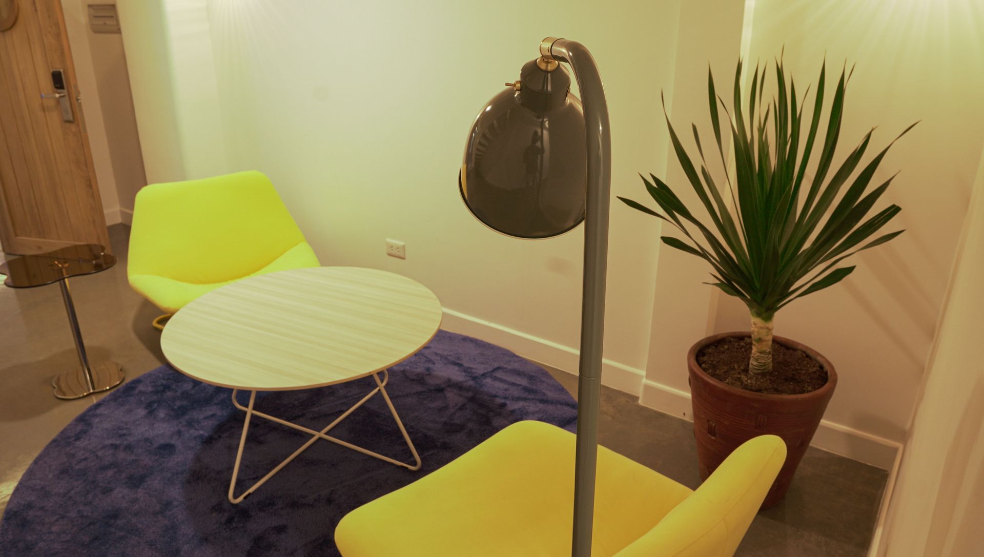 Small seating area with yellow chairs, a round table, and a potted plant, illuminated by a floor lamp.