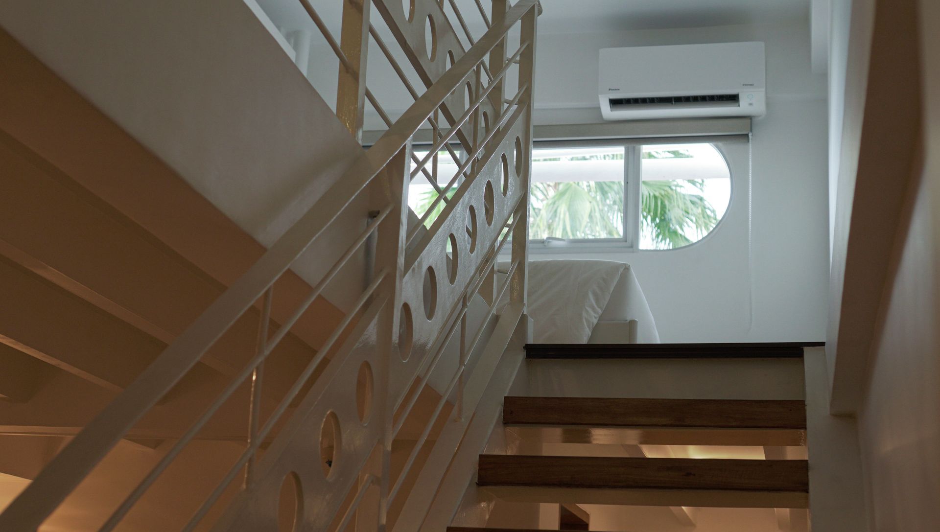 White staircase with a metal railing. A window and air conditioner are at the top, a bed is visible through the window.