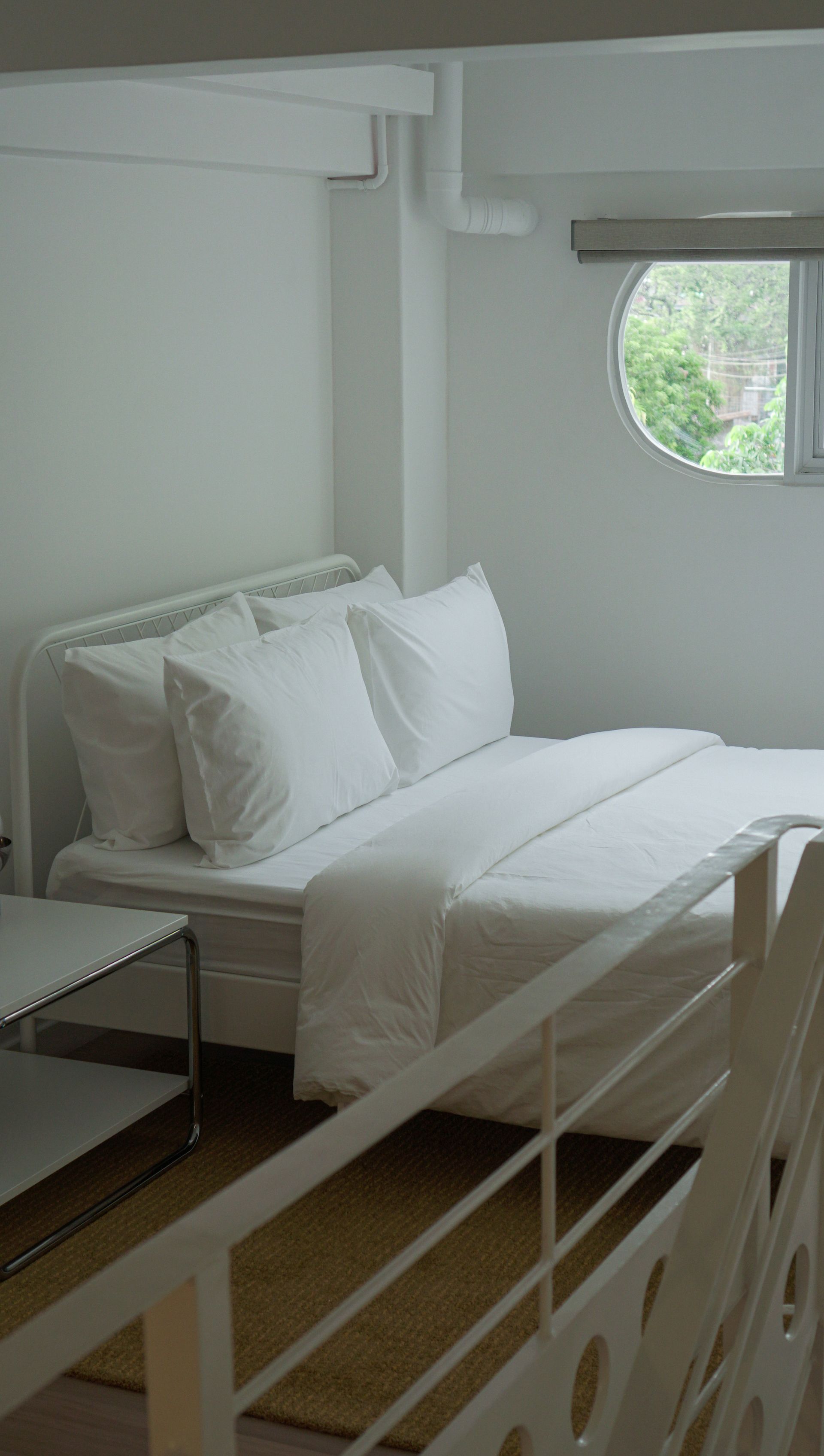 White bedroom with bed, pillows, window, and a loft railing.