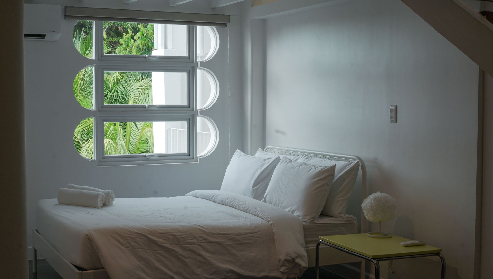 White bedroom with bed, round window, and side table.