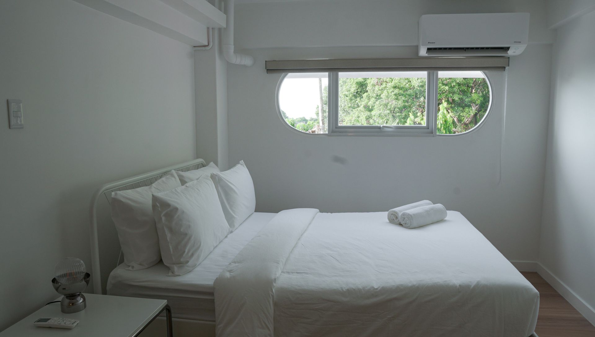 White bedroom with a bed, small nightstand, window, and air conditioner.