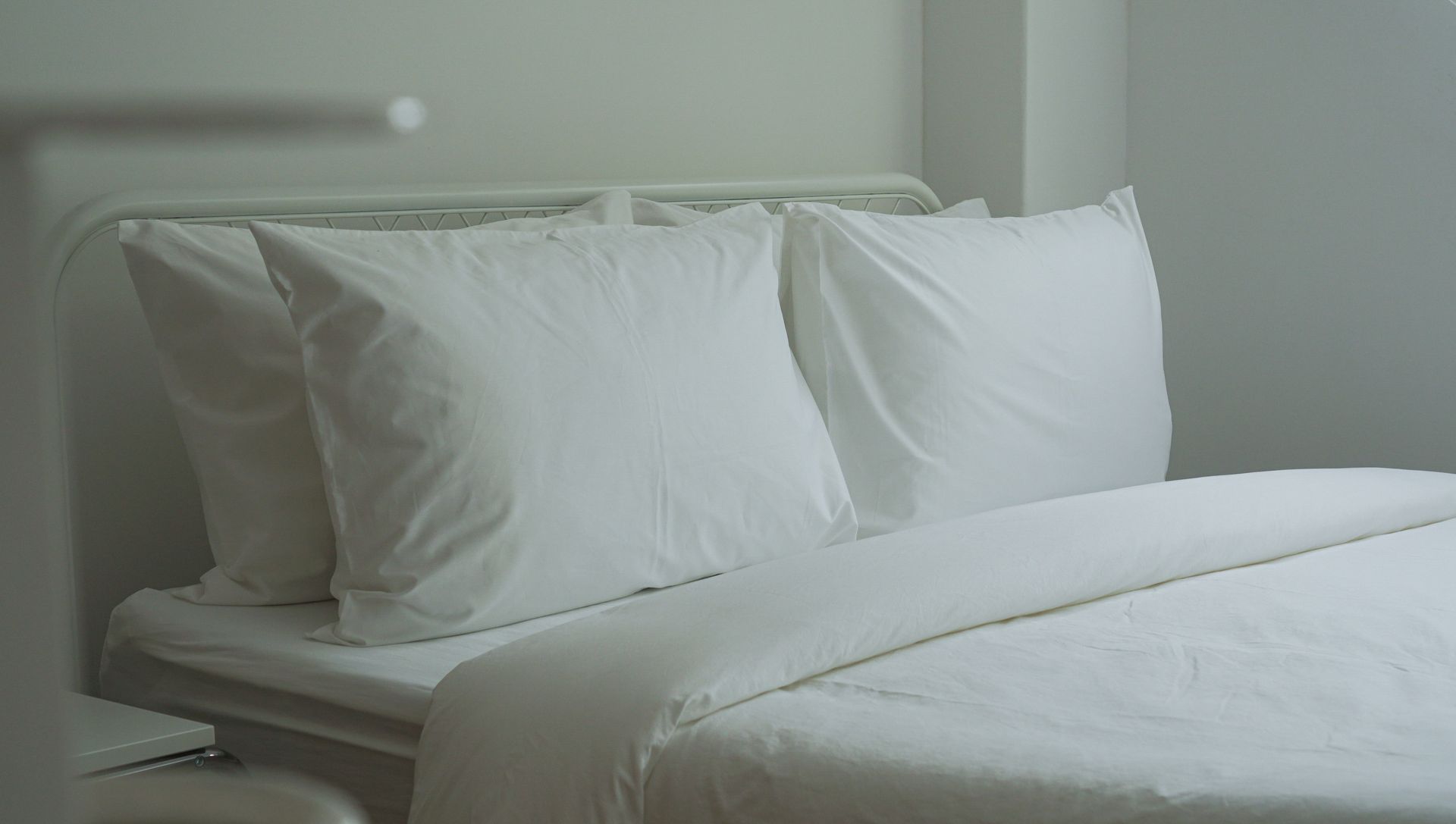 White bed with pillows and duvet, in a bright room.