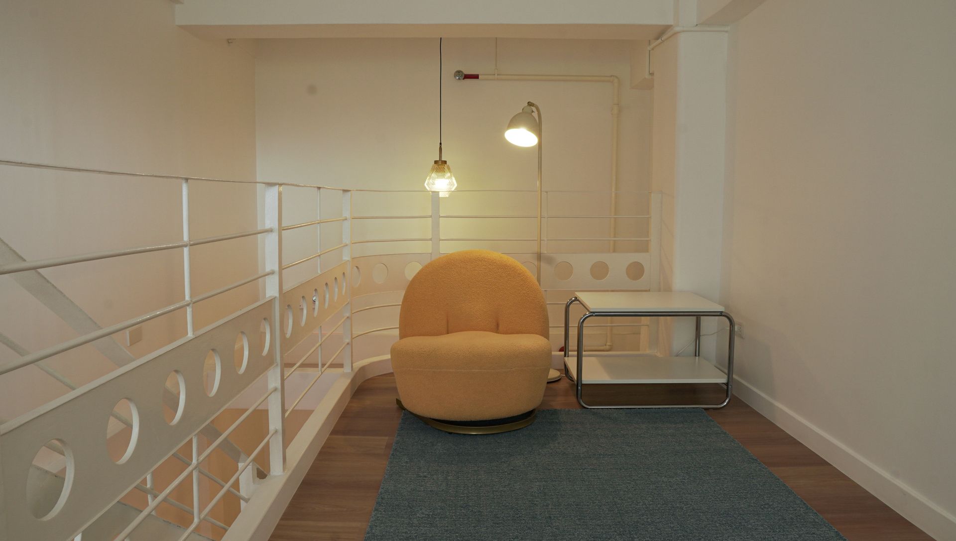 Yellow armchair in a reading nook with rug, side table, and two hanging lights.