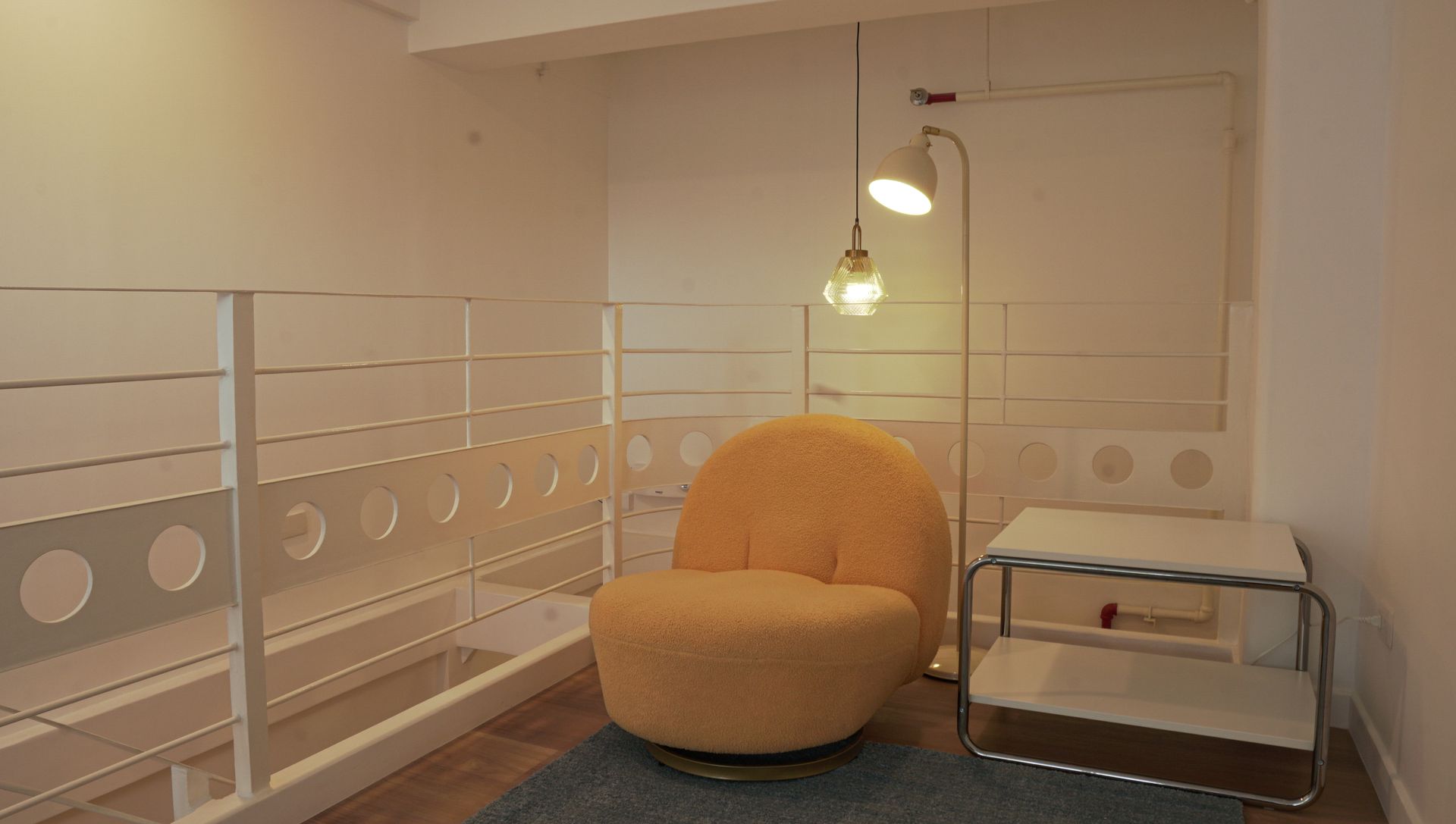 Yellow armchair and lamp in a bright reading nook with white railing and side table.