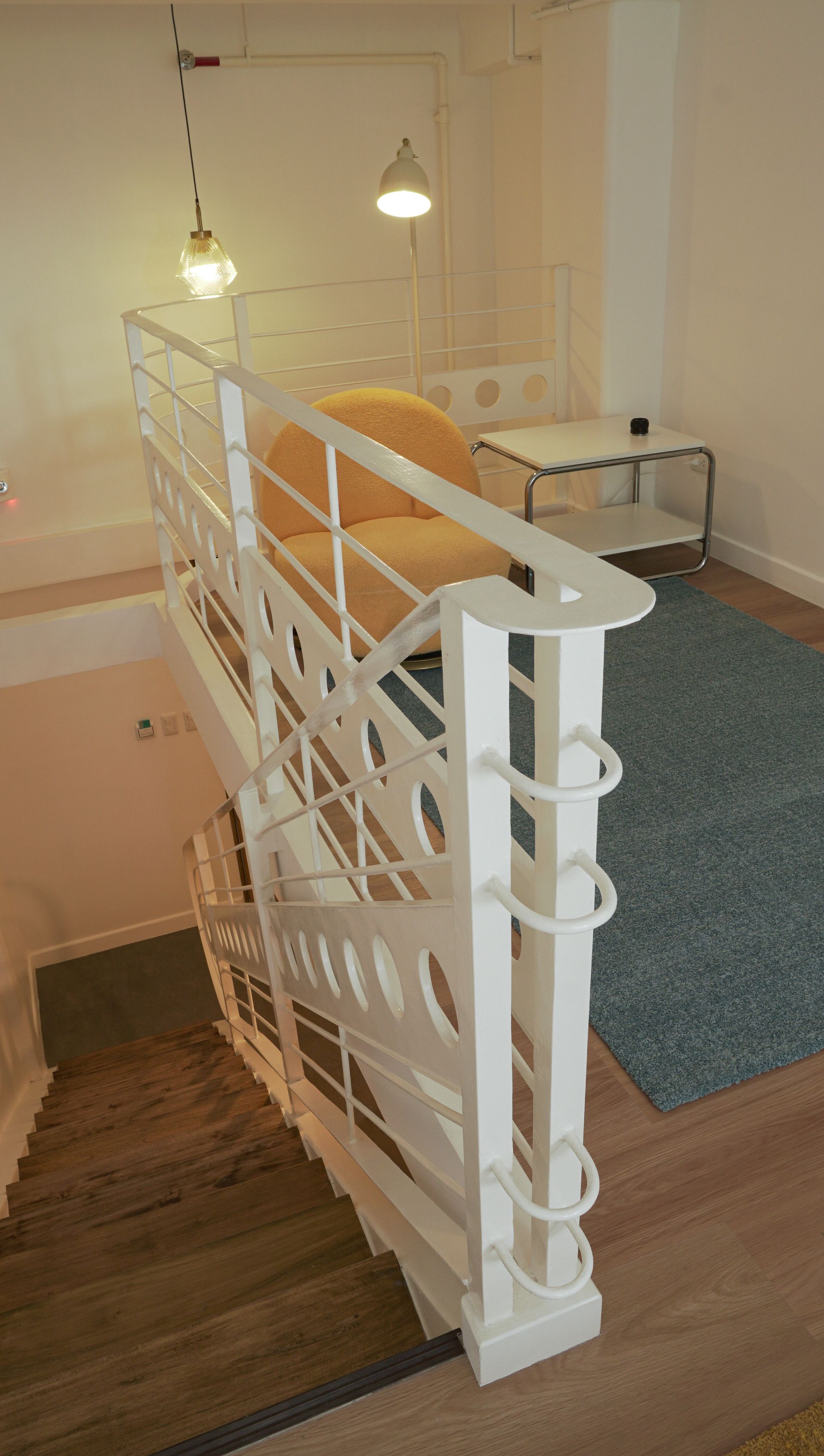 White stair railing with circular cutouts, leading up to a seating area with yellow cushion and rug.
