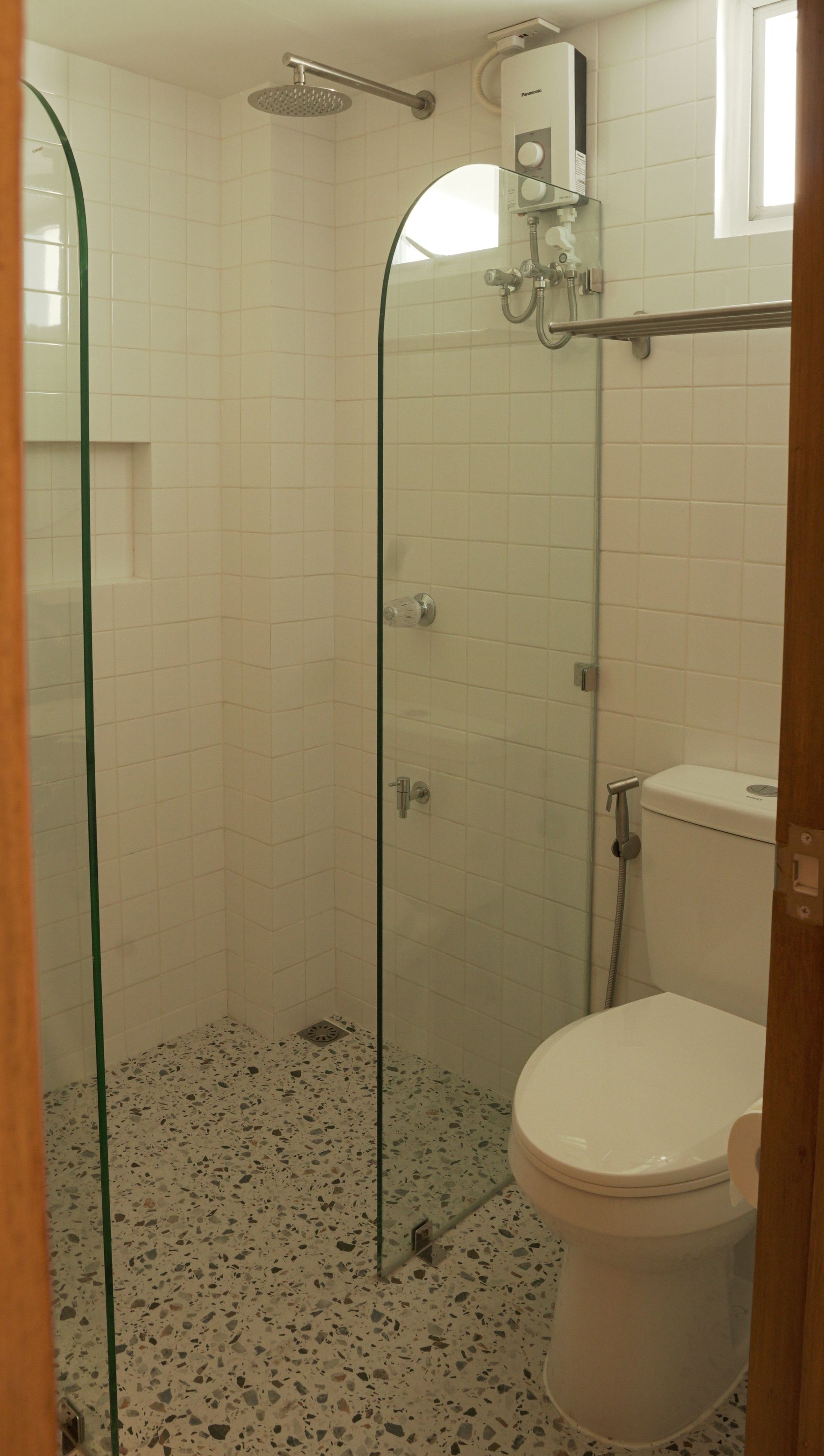 Bathroom with white tiled walls, glass shower door, and a toilet.