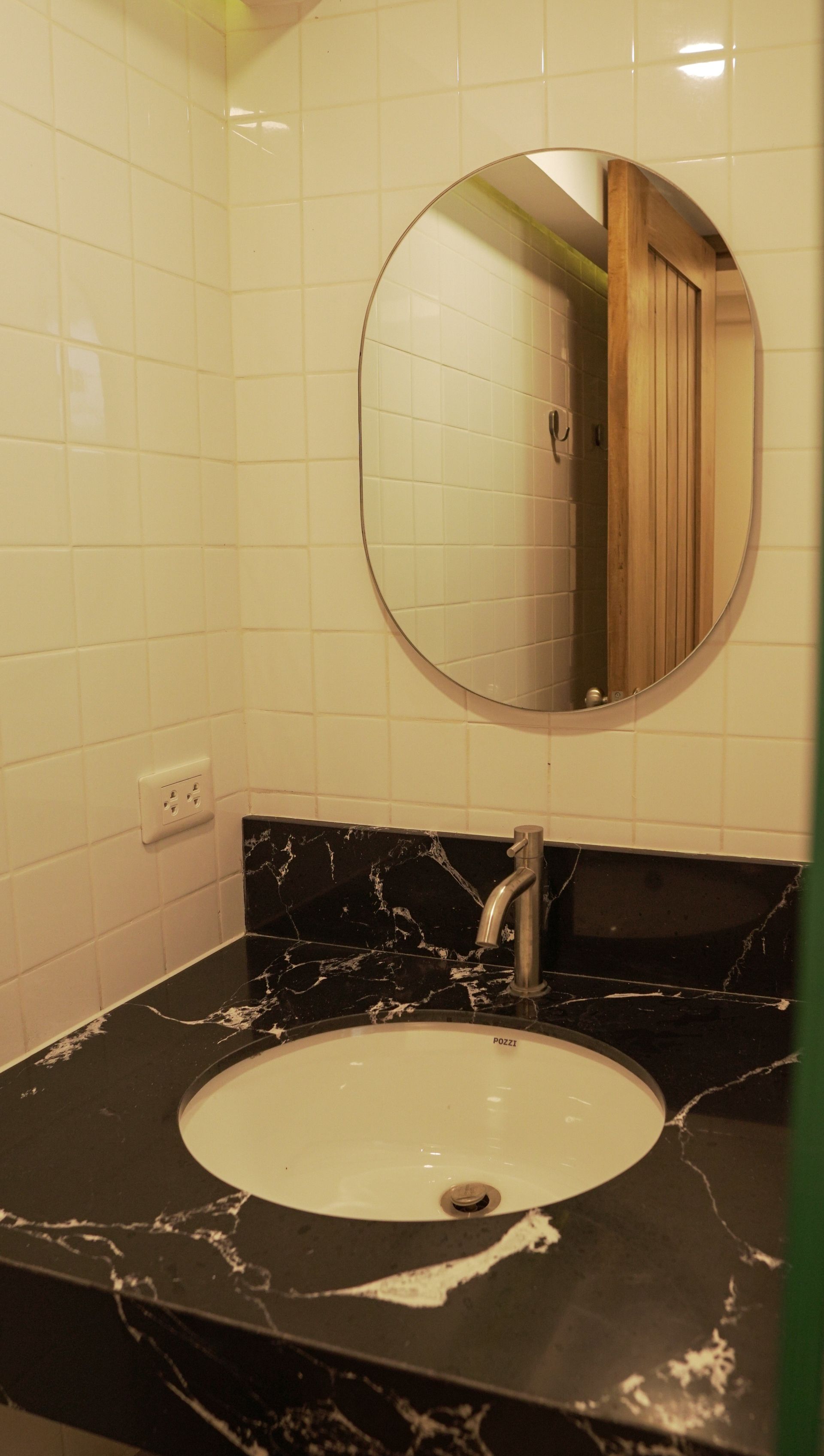 Bathroom sink with oval mirror above, black marble countertop, white tile walls.