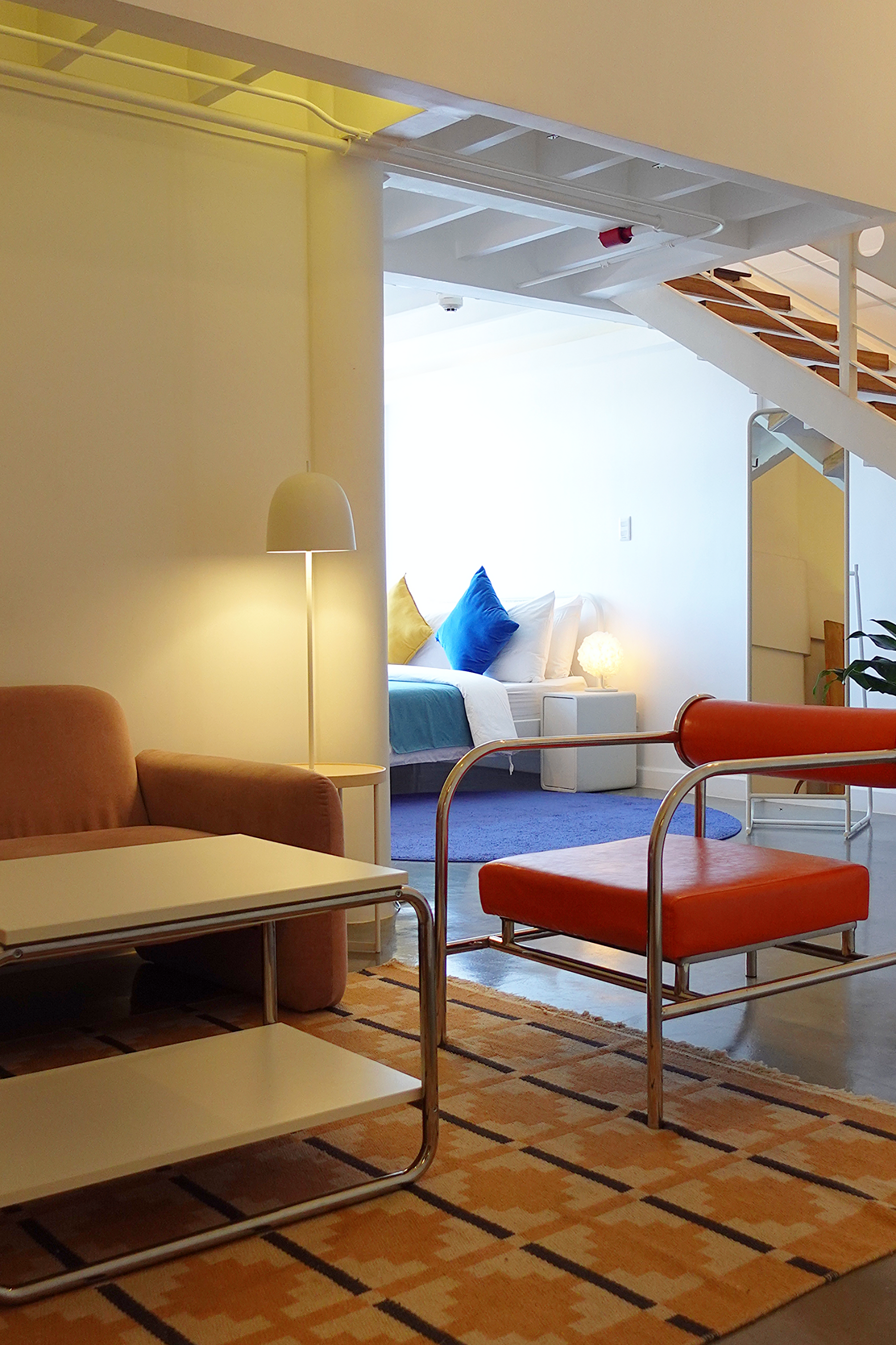 Living room with orange chair, white table, and view into bedroom with blue pillows.