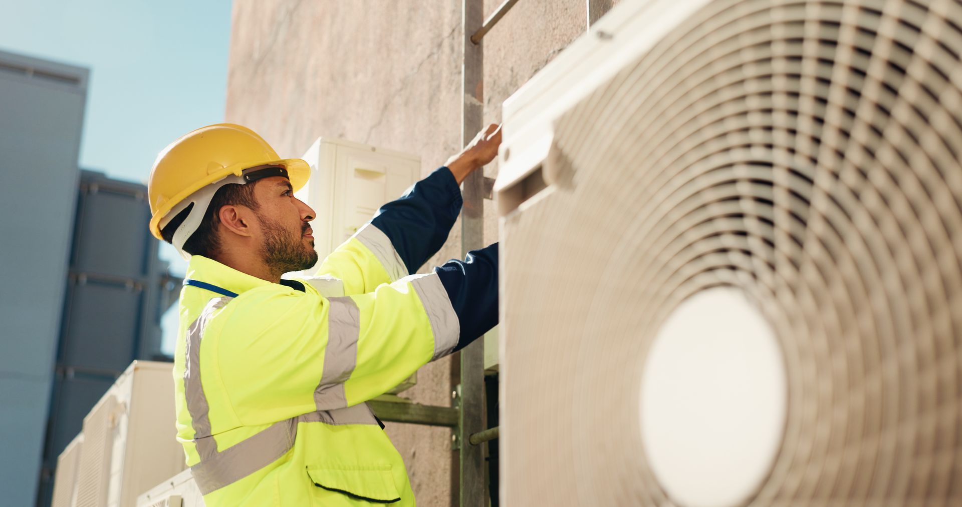 Technician in yellow safety gear inspecting an outdoor HVAC unit near a building wall Technician in yellow safety gear inspecting an outdoor HVAC unit near a building wall