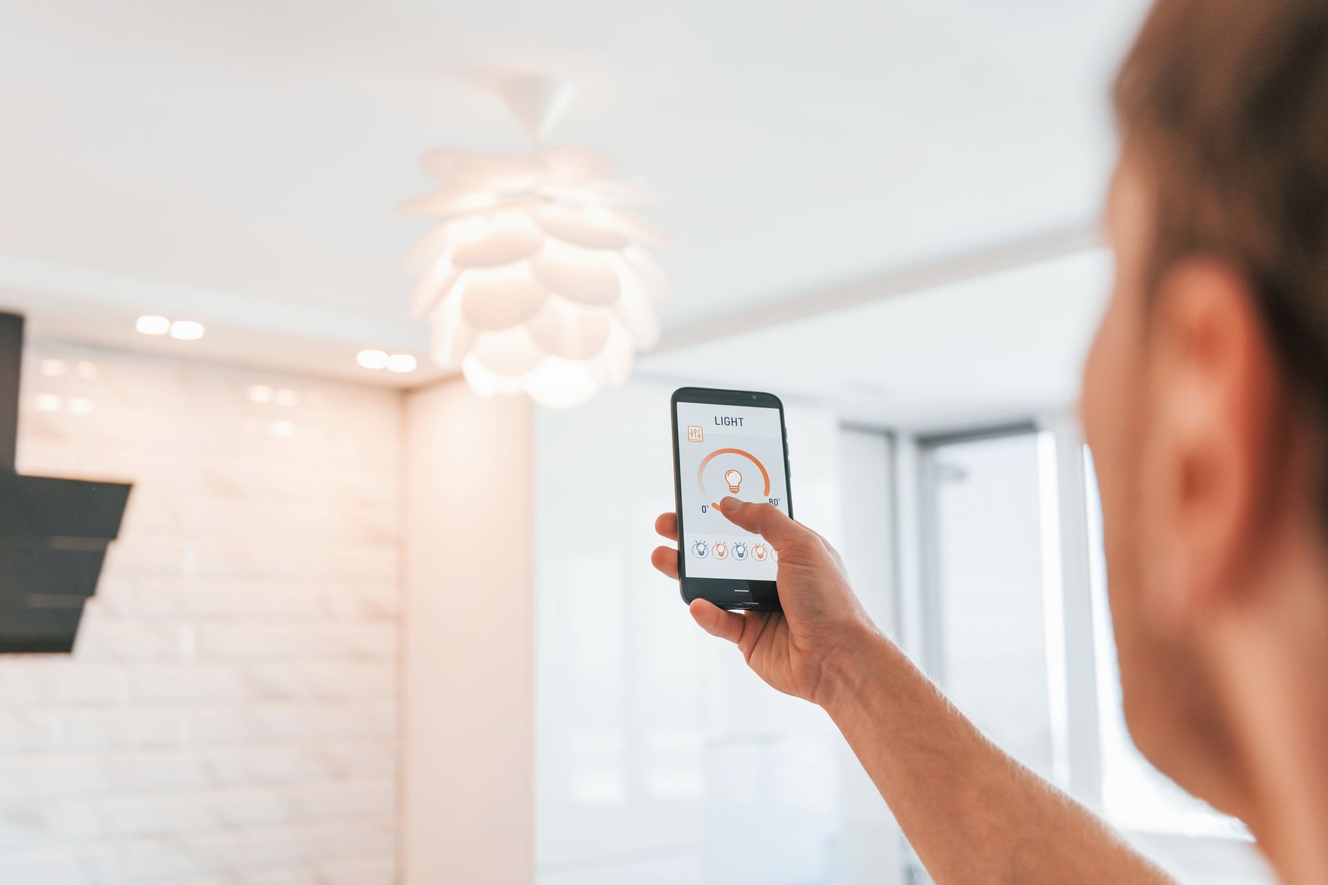 A partial view of a man that is indoors controlling his lighting through smart home technology.