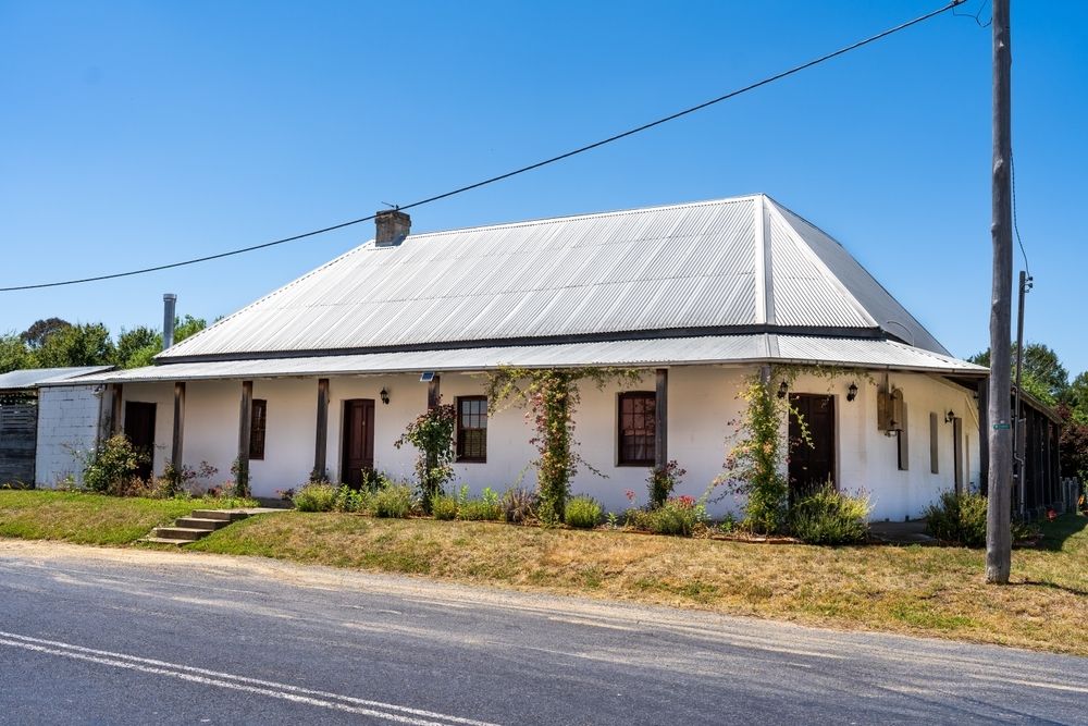 A White House With a Metal Roof is Next to a Road — Sheps Roofing Service Pty Ltd In Gerrigong, NSW