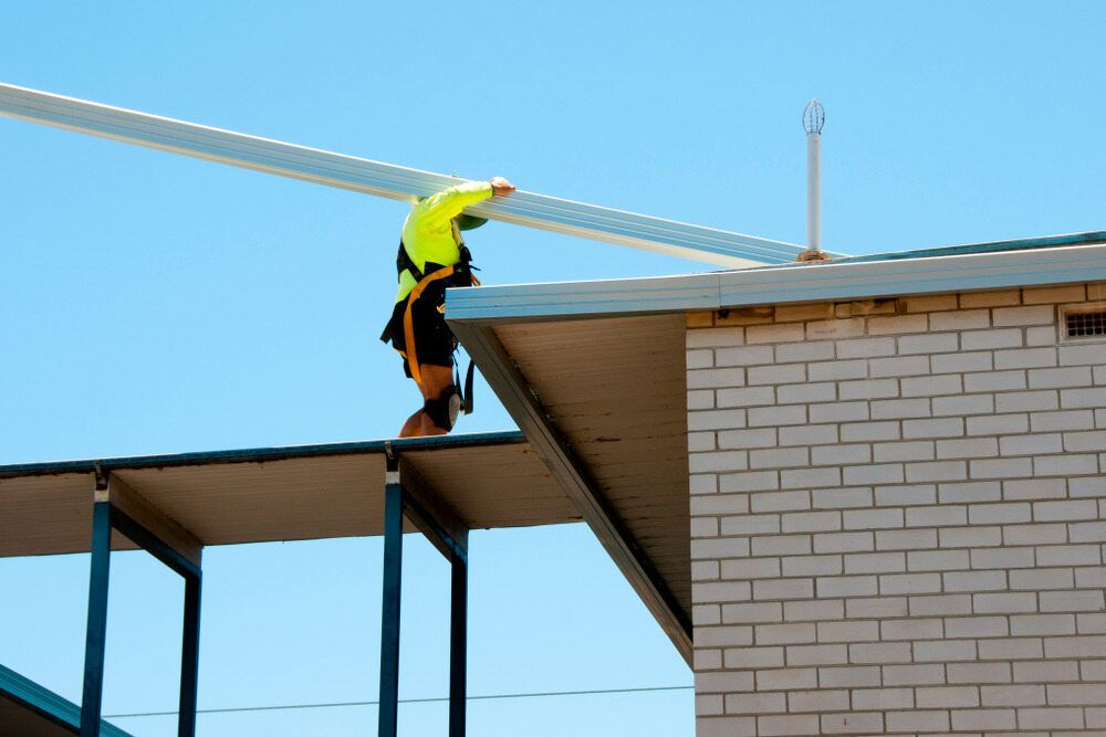 A Man is Working on the Roof of a Building — Sheps Roofing Service Pty Ltd In Albion Park, NSW
