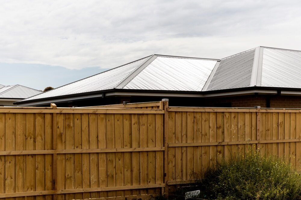 A Wooden Fence Surrounds a House With a White Roof — Sheps Roofing Service Pty Ltd In Kiama, NSW