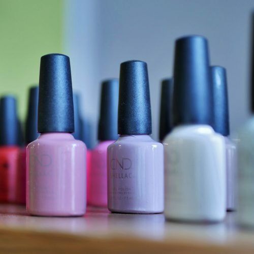Reihen von rosa, lila und weißen Nagellackfläschchen mit schwarzen Verschlüssen.
