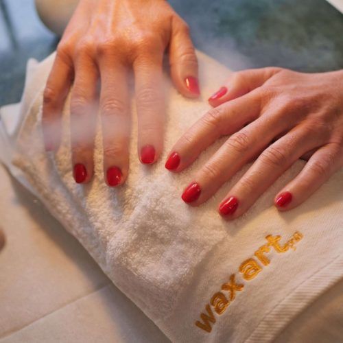 Hände mit rotem Nagellack, die auf einem weißen Handtuch mit der Aufschrift 