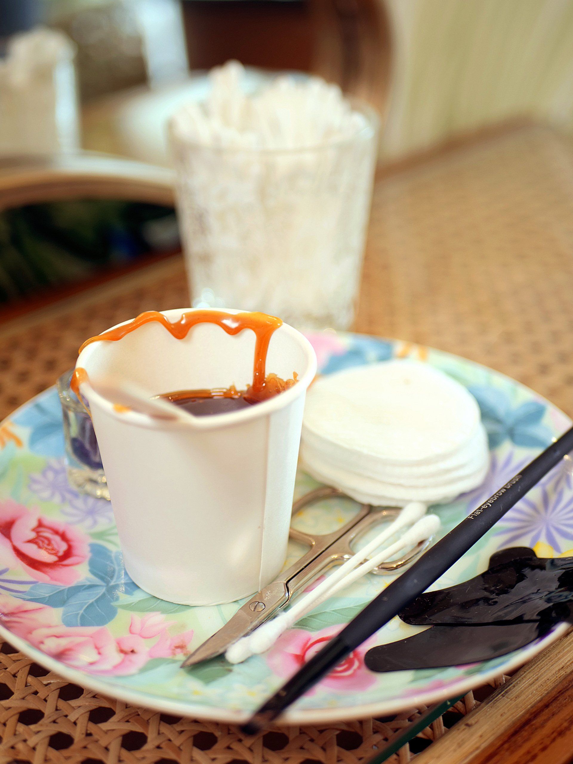 Kaffee mit Karamellsoße, Wattepads, Werkzeug und Schlagsahne auf einem blumengemusterten Teller.