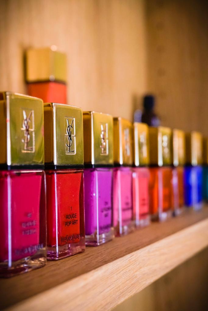 Eine Reihe bunter Nagellackfläschchen mit goldenen Deckeln auf einem Holzregal.