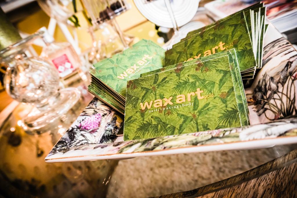 Ausgestellt sind Visitenkarten mit dem Schriftzug „Wax Art“ auf grünem, blattartigem Hintergrund.