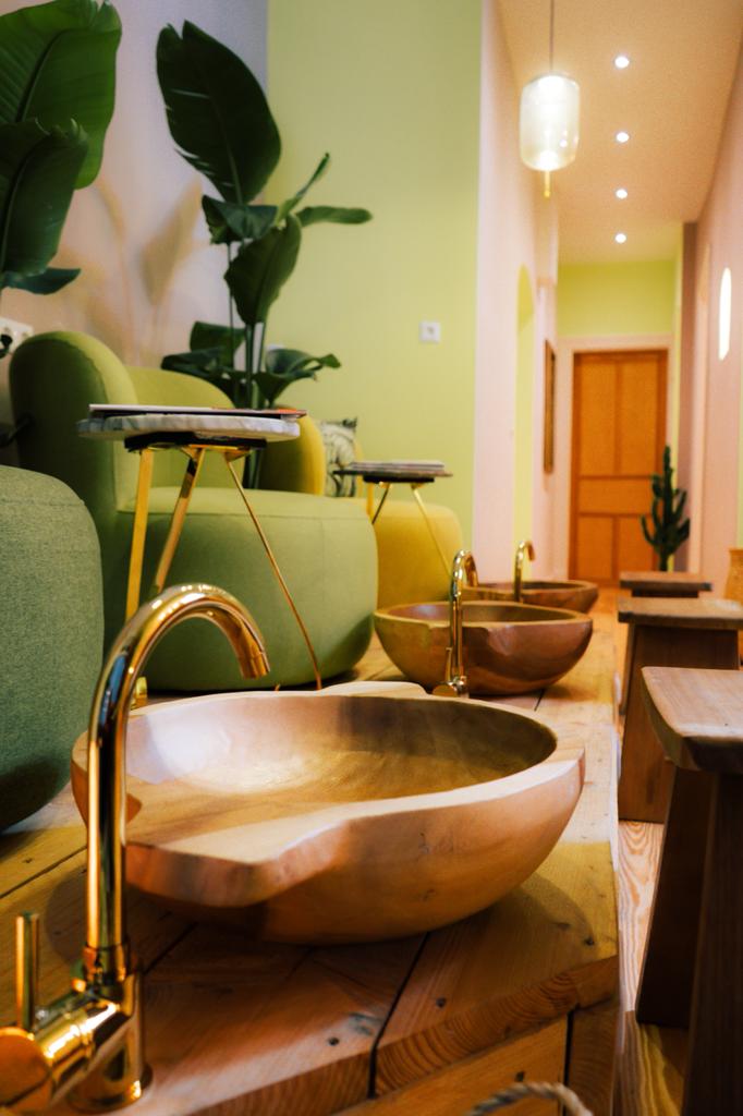 Holzwaschbecken mit goldenen Armaturen in einem Wellness-Ambiente, mit grünen Möbeln und Pflanzen.