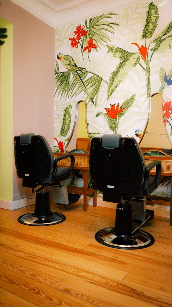 Zwei Friseurstühle in einem Salon mit tropischer Tapetentapete und Holzboden.