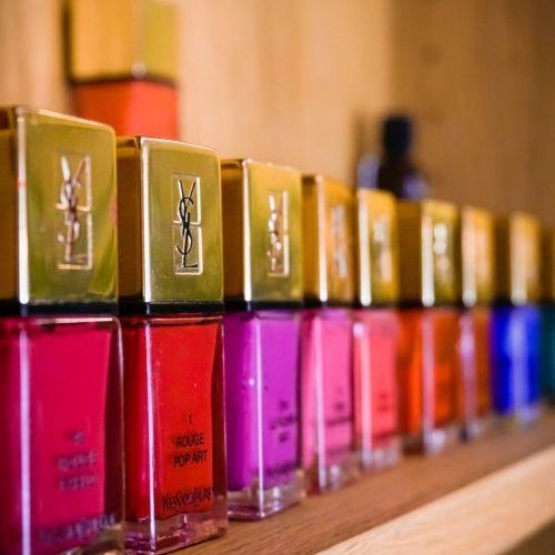 Eine Reihe von bunten Nagellackfläschchen mit goldenen Verschlüssen auf einem Holzregal.