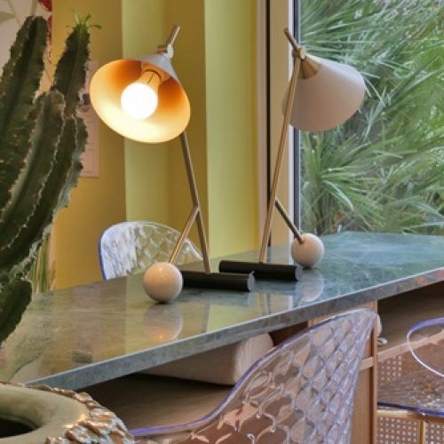 Zwei moderne Tischlampen auf einem Marmortisch; eine davon ist beleuchtet. Im Hintergrund ein Kaktus und ein Fenster.