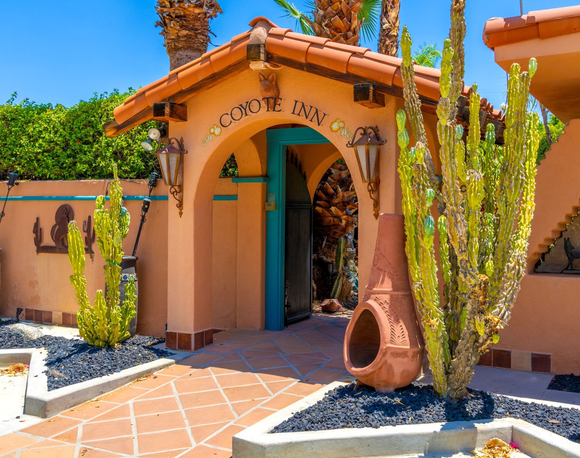Coyote Inn entryway with terracotta roof, teal door, cactus, and decorative urn.