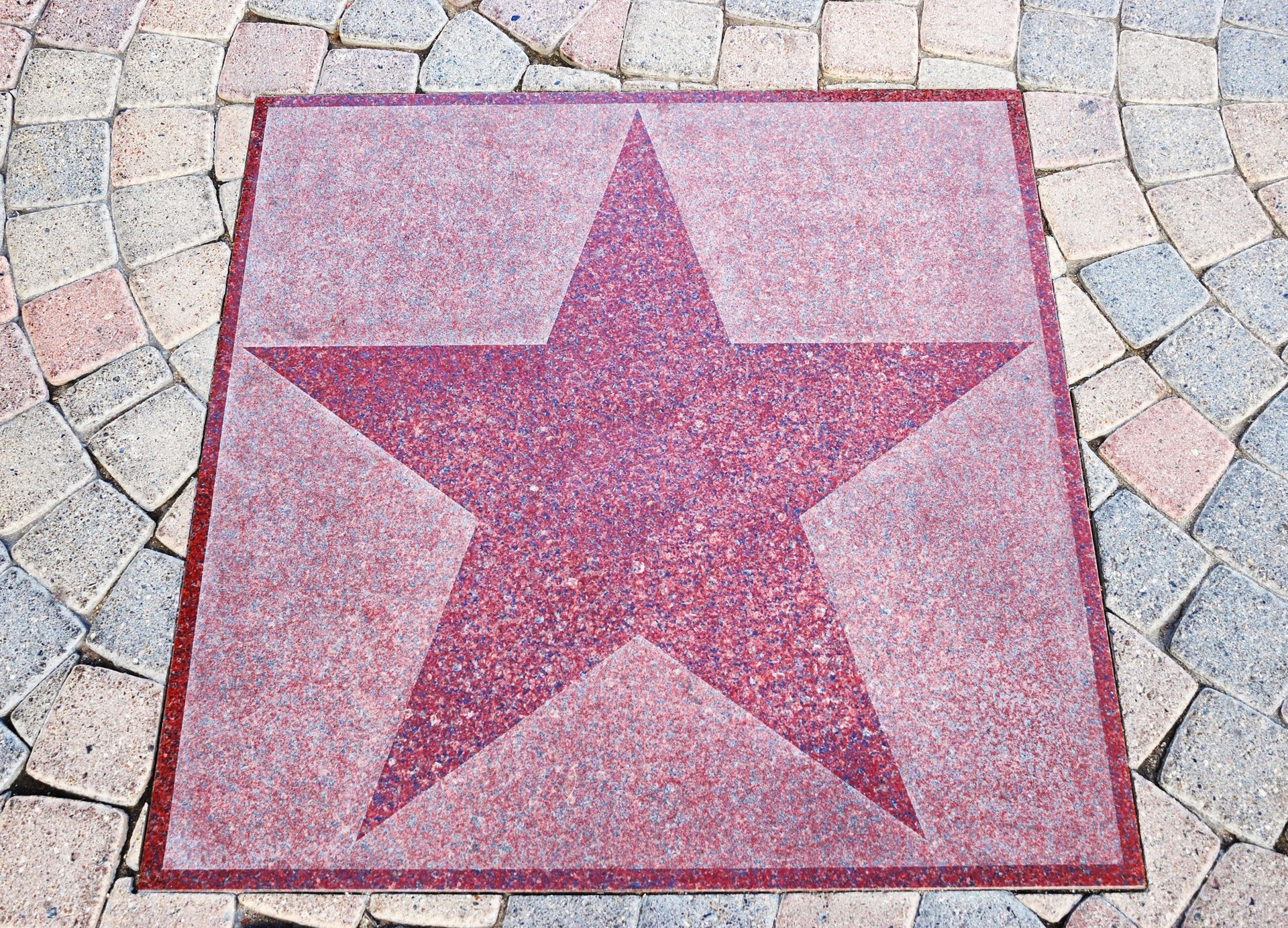 Red terrazzo star embedded in sidewalk, surrounded by cobblestones.