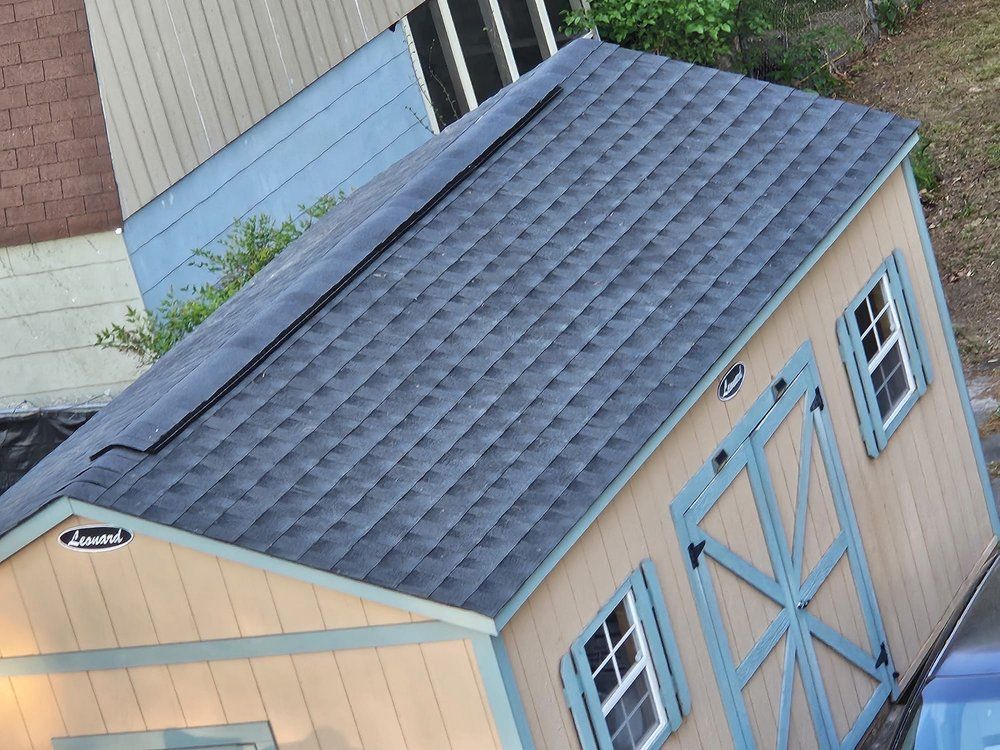 Blue-roofed wooden storage shed with double doors beside a brick house.