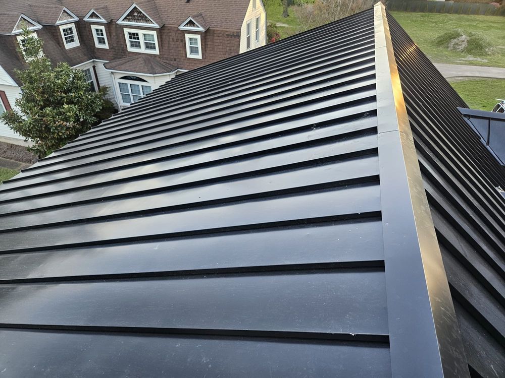 Black metal standing-seam roof on a house, viewed from above with neighboring homes in the background