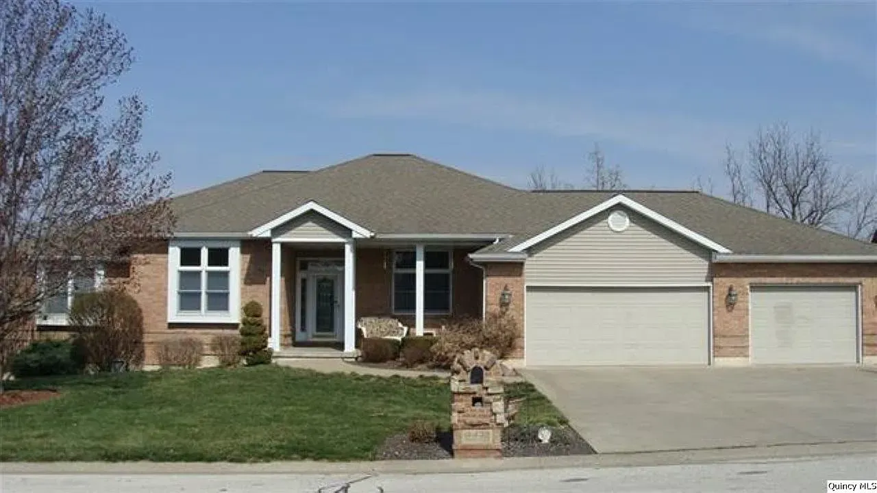 Brick ranch-style house with a gray roof and a three-car garage. The front door is white with a small window, and there's a green lawn.