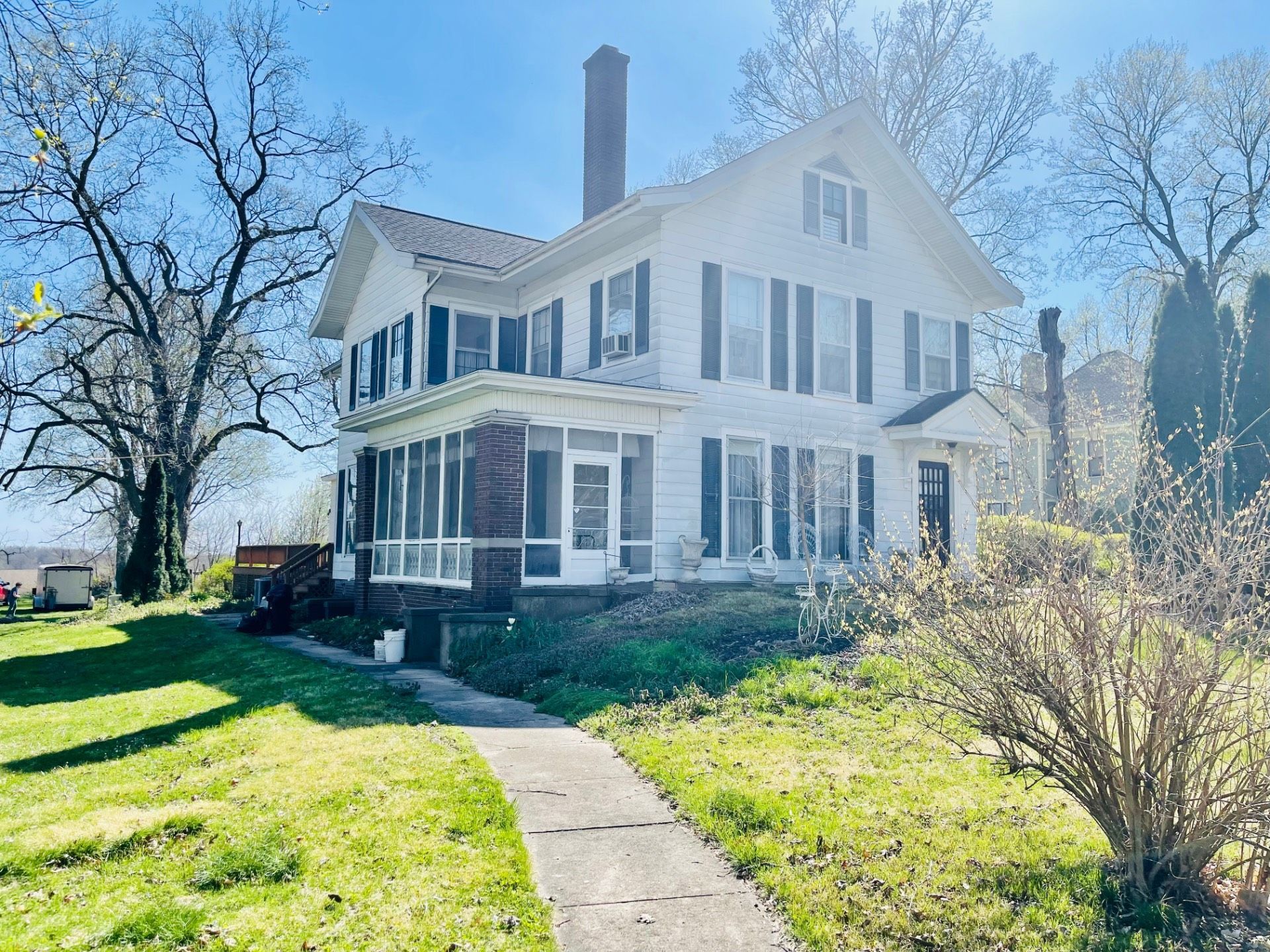 White two-story house with black shutters and a screened-in porch. A pathway leads to the front door