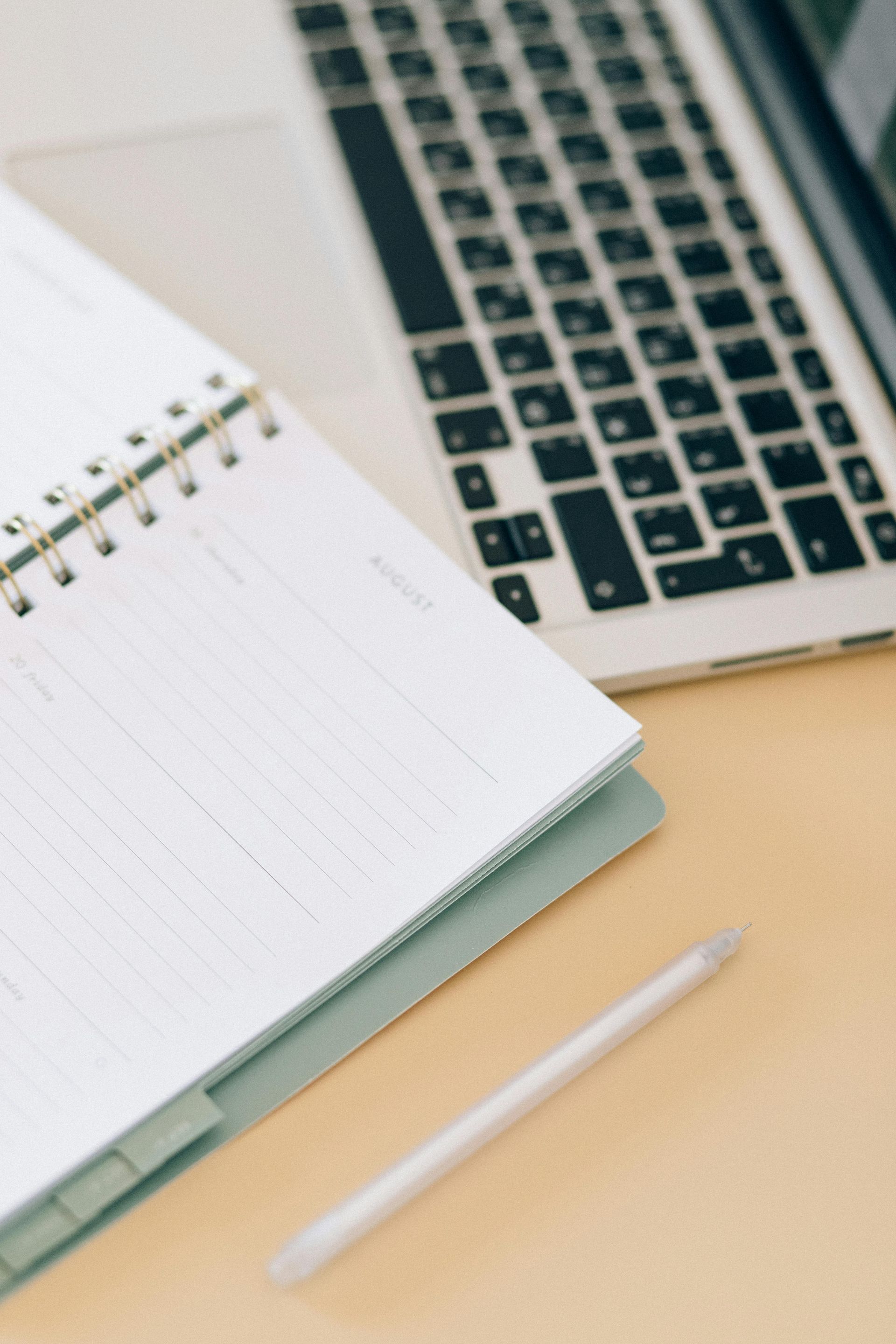 Open notebook and laptop with pencil on a light-colored desk, ready for work.