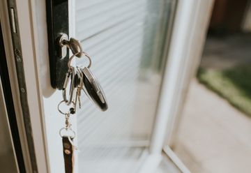 Keys hanging in a door lock, with a white frame and a window in the background.