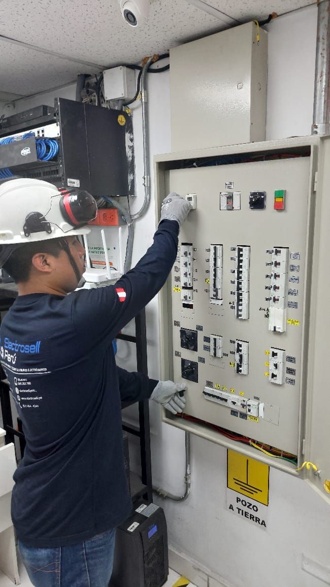 Técnico con casco de seguridad inspeccionando un panel de control eléctrico con interruptores y etiquetas.