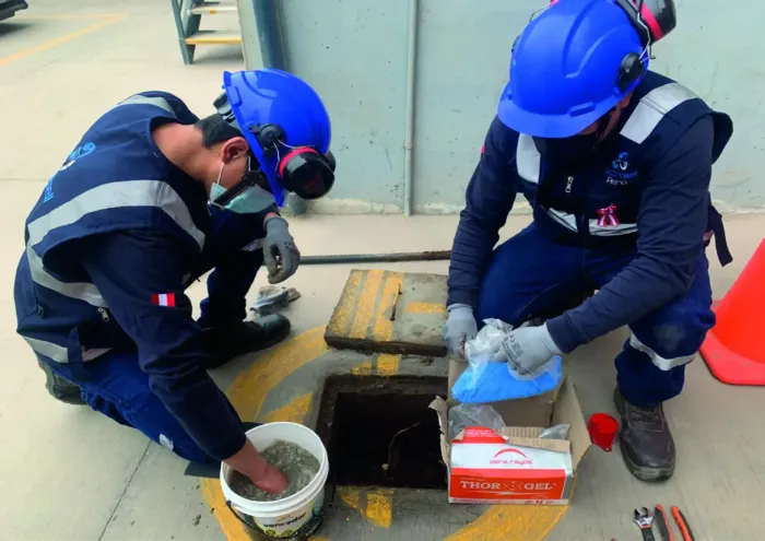 Dos trabajadores con equipo de seguridad azul inspeccionan una alcantarilla abierta en una obra