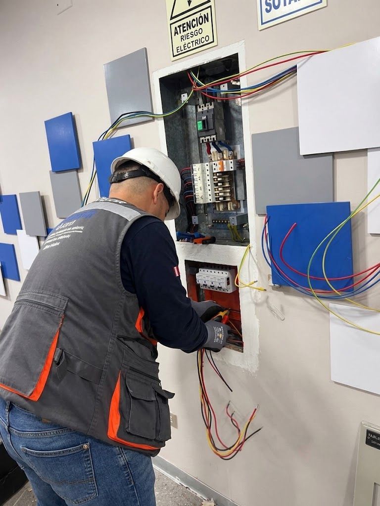 Un trabajador con casco ajustando el cableado dentro de un cuadro eléctrico abierto en la pared.