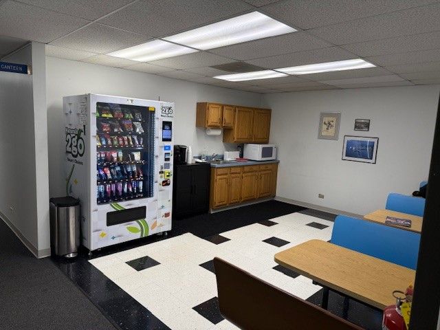 Break room with vending machine, cabinets, sink, tables and blue chairs on a black-and-white tiled floor