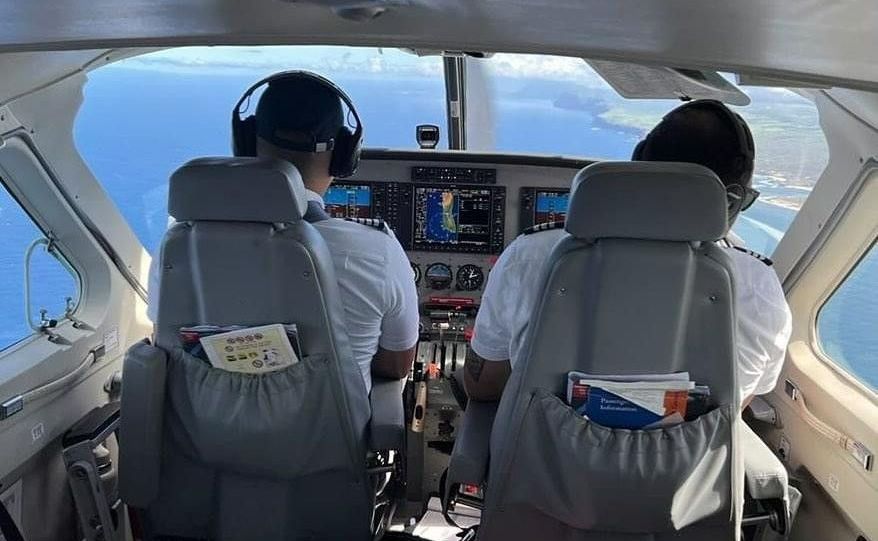 Two pilots operating a Cessna Caravan with glass cockpit displays while flying over the coastline.