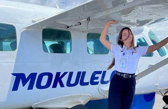 Pilot standing beside Mokulele Airlines aircraft, smiling and posing under the wing.