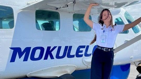 Pilot standing beside Mokulele Airlines aircraft, smiling and posing under the wing.