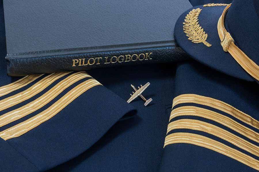 Pilot logbook with captain’s uniform, hat, and gold aviation stripes displayed together.